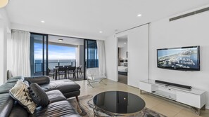 A modern living room with a sofa, a coffee table, a TV mounted on the wall, and a balcony with a view of the sea. - Esplanade (Soul), Apartment 5004 + 5005 (Surfers Paradise)