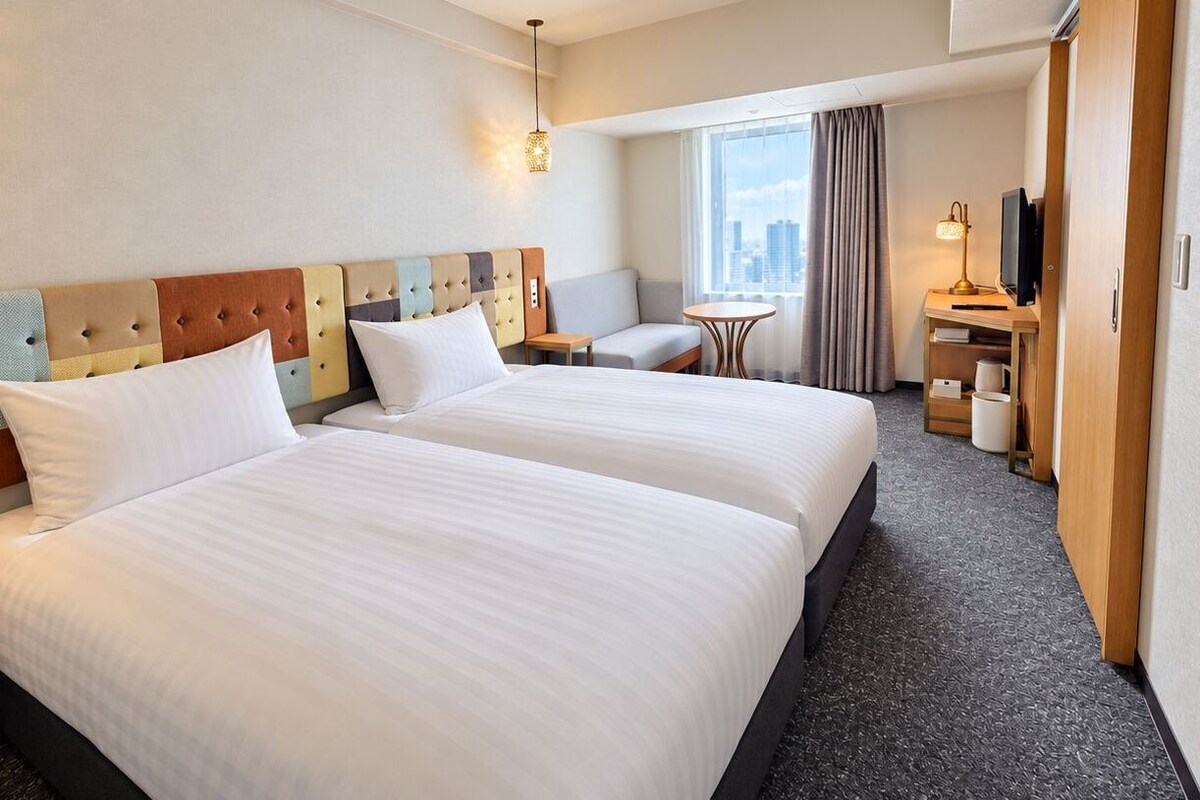 A hotel room with two beds, a seating area, a television, and a window with a view.