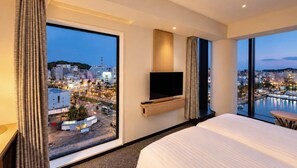 A hotel room with a bed, a TV mounted on the wall, and large windows offering a city view. - Hotel nostal TOKUSHIMA (tokushimashi)