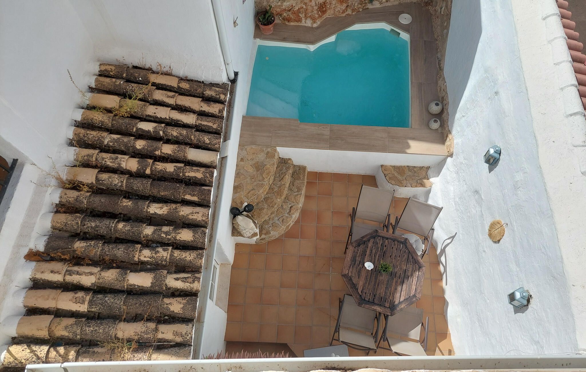 Eine Dachterrasse mit Schwimmbad, Tisch und Stühlen sowie einer Steinmauer.