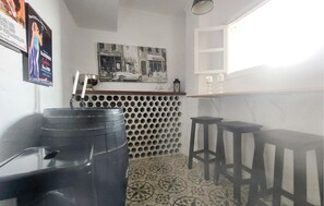 Una habitación pequeña y compacta con piso estampado, una zona de bar con taburetes, un estante en la pared y un cuadro enmarcado sobre la barra.