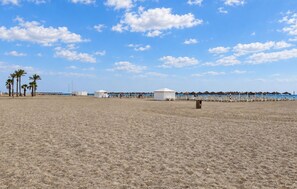 Ein Strand mit Zelten und Sonnenschirmen, Palmen und blauem Himmel.