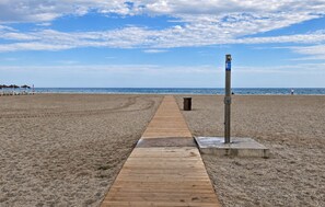 Ein hölzerner Steg führt zum Strand, mit einer Mülltonne und einem Wegweiser.
