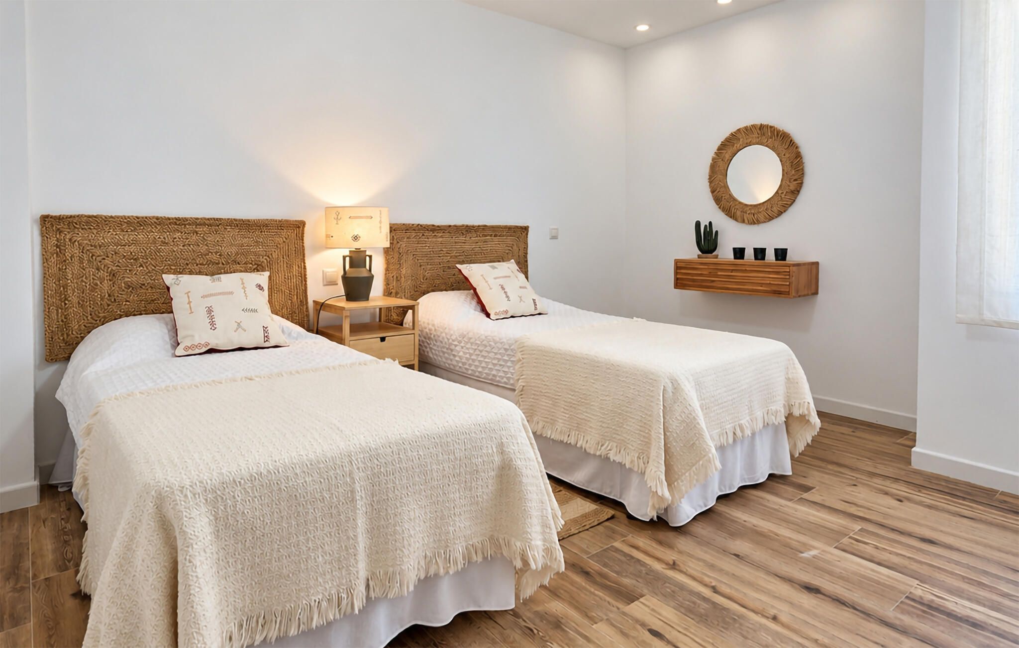 Een hotelkamer met twee bedden, een nachtkastje met lamp, een spiegel aan de muur en een houten plank met decoratieve objecten.