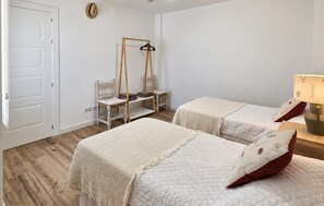 Ein Schlafzimmer mit zwei Betten, Holzboden, einem Sessel, einem hölzernen Kleiderbügel und einer Lampe.