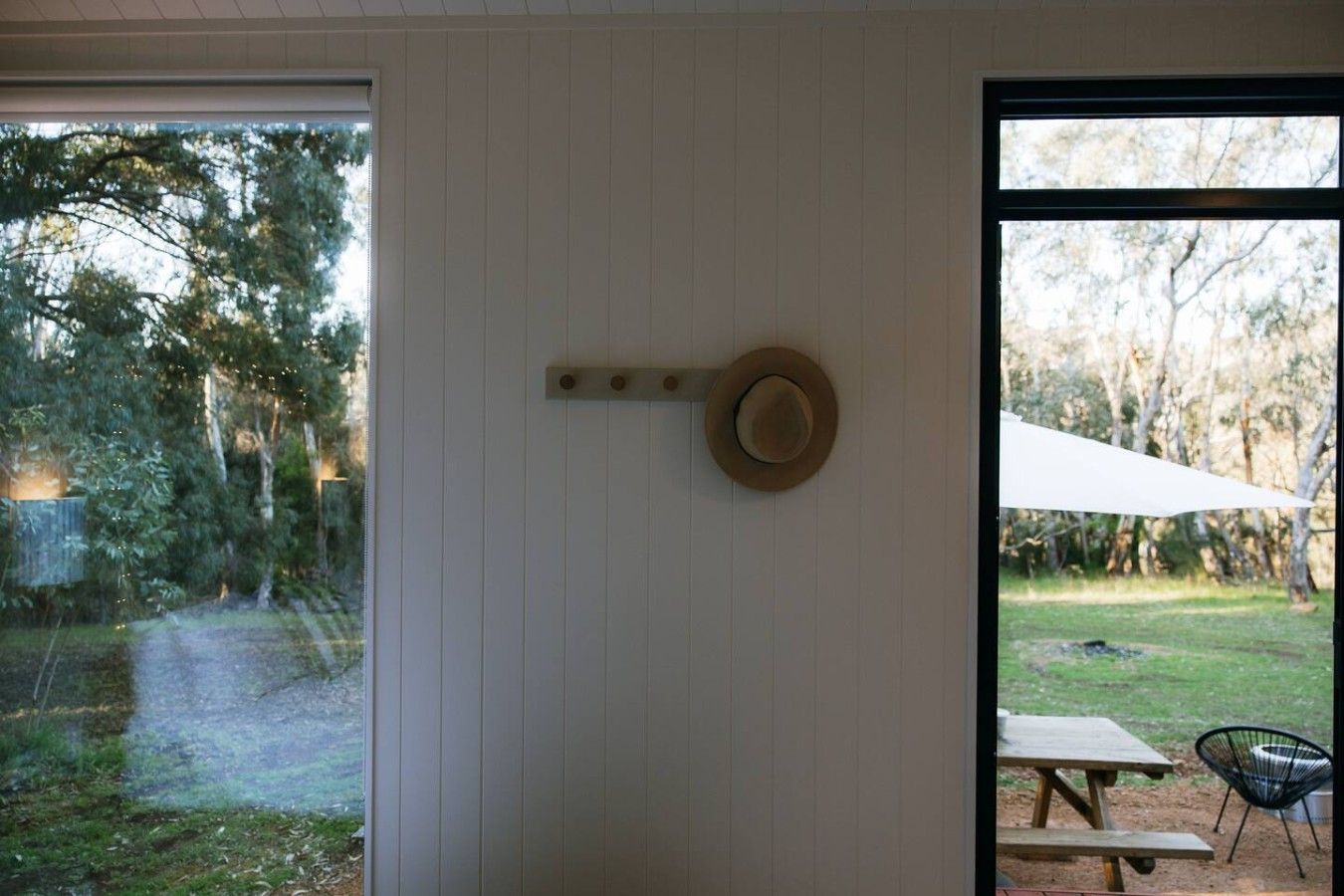 A room with a large window, a hat hanging on the wall, and a view of a grassy area with trees.