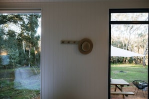 Una habitación con un ventanal grande, un sombrero colgado en la pared y vista a un área verde con árboles.