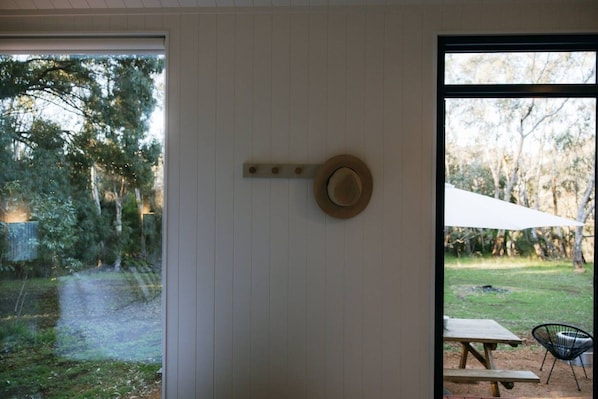 A room with a large window, a hat hanging on the wall, and a view of a grassy area with trees.