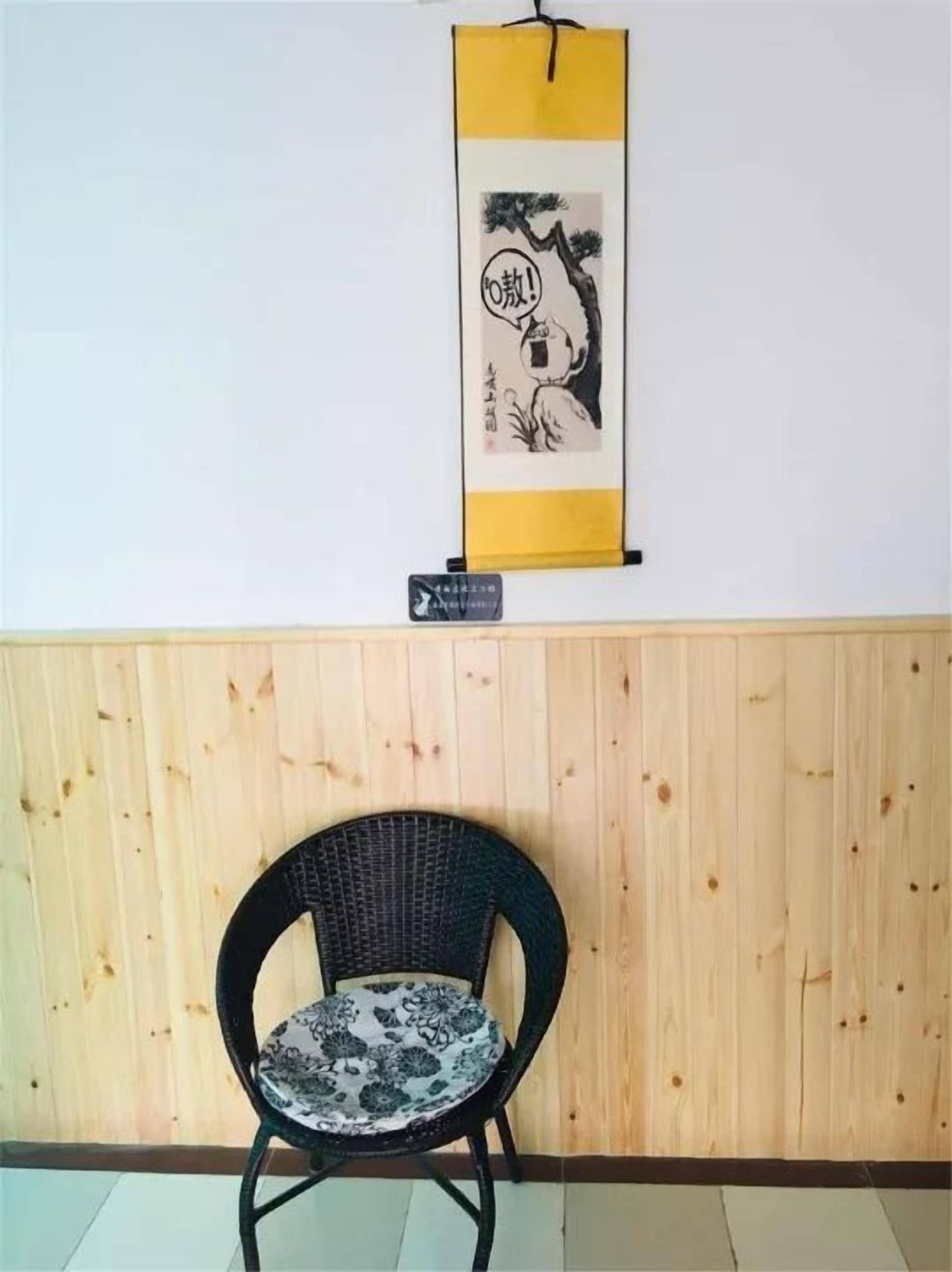 A black wicker chair with a patterned cushion against a wooden wall, a vertical yellow and white sign with Japanese characters, and a small black sign below the chair.