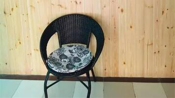 A black wicker chair with a patterned cushion against a wooden wall, a vertical yellow and white sign with Japanese characters, and a small black sign below the chair.