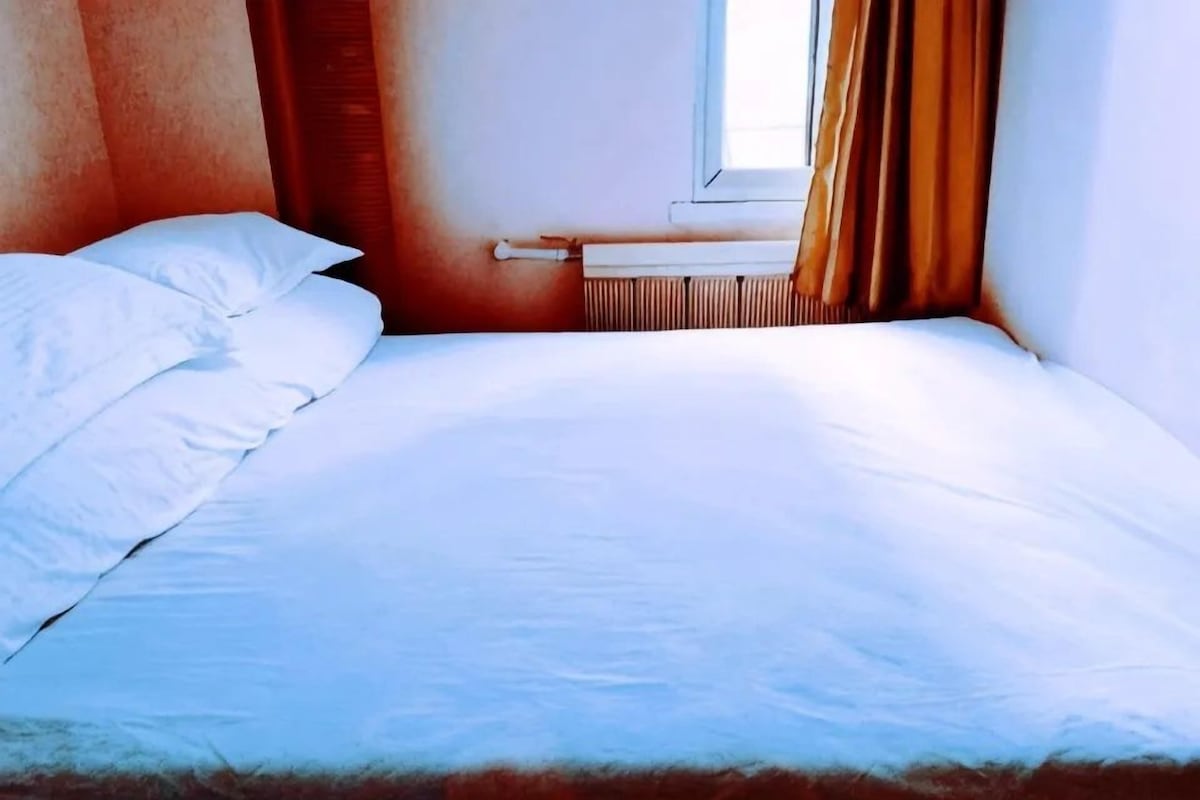 A bed with white linens in a room with a window and curtains.