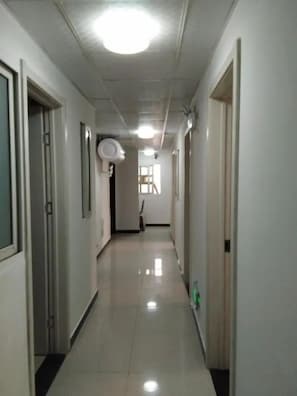 Un pasillo largo y estrecho con puertas a ambos lados, una lámpara en el techo y una ventana al final.