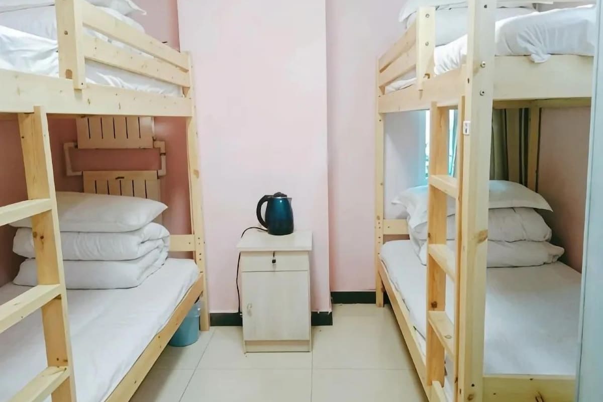 A room with bunk beds, a small bedside table with a kettle, and a cabinet.