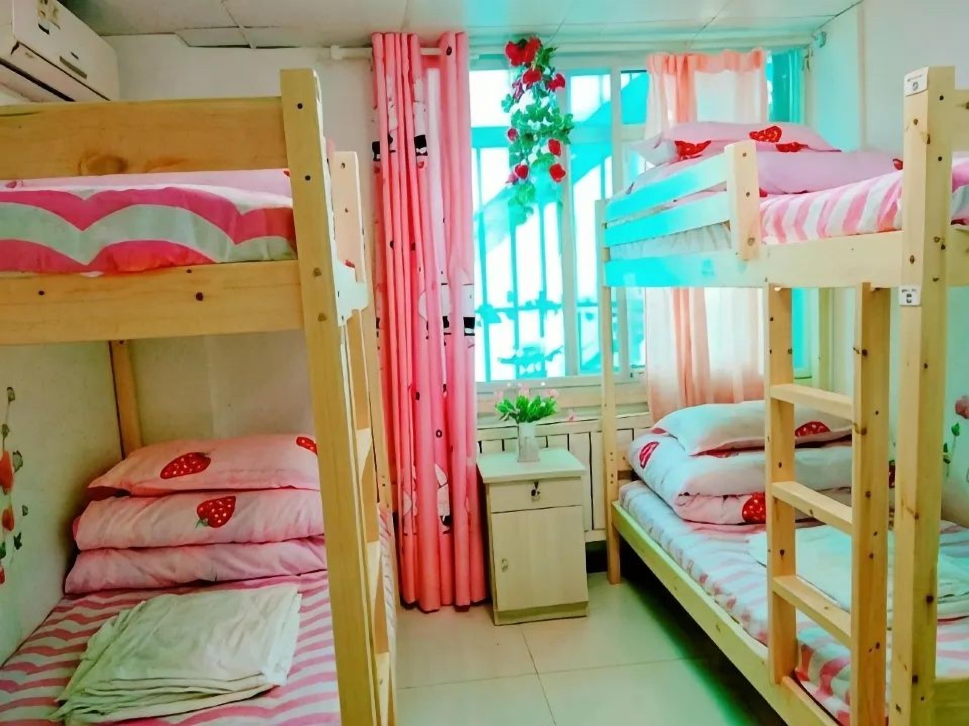Habitación con literas, ropa de cama rosa, una mesita de noche pequeña y una ventana con cortinas.