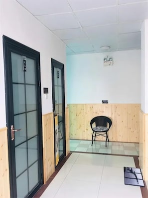Un pasillo con piso de madera, una silla negra y una puerta con paneles de vidrio esmerilado.