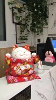 Una mesa de recepción con una figura decorativa de gato, una pequeña figurina blanca y una pantalla digital.