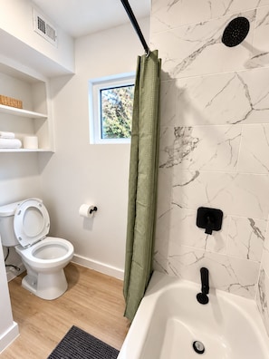 Une salle de bain avec des toilettes, un rideau de douche, une baignoire et une fenêtre.