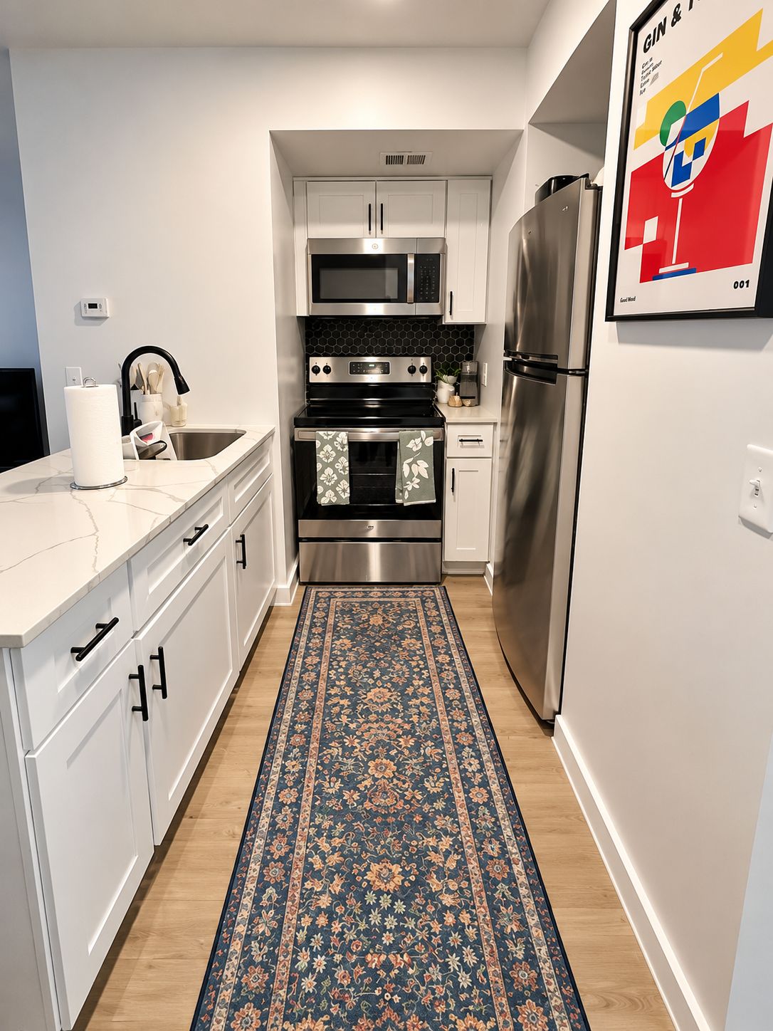 Une cuisine moderne avec des meubles blancs, des appareils en acier inoxydable et un tapis à motifs bleus.