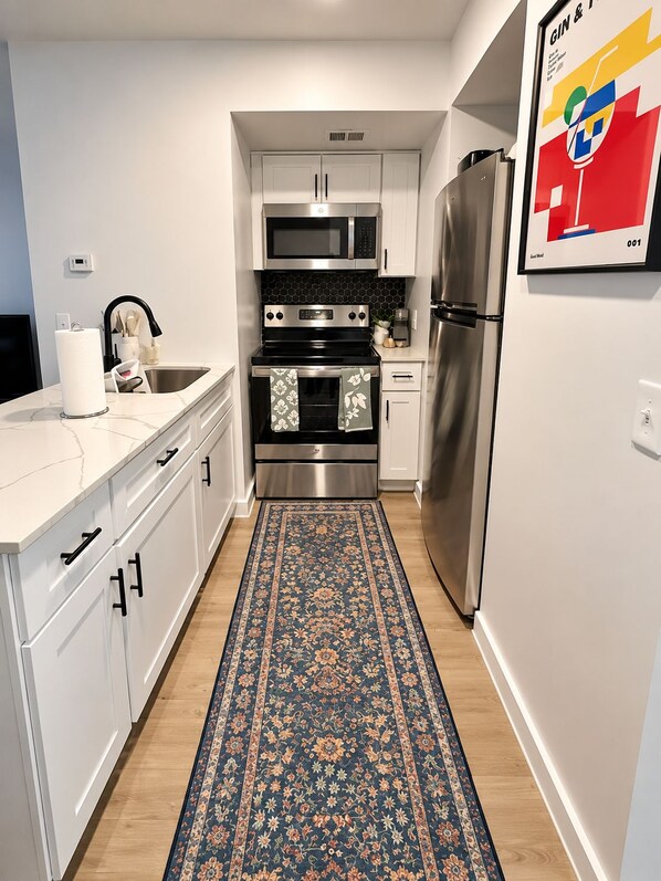 A modern kitchen with white cabinetry, stainless steel appliances, and a blue patterned rug.