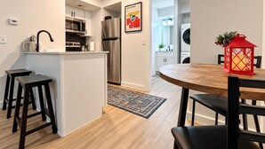 Cuina moderna amb illa central, electrodomèstics d'acer inoxidable i zona de menjador amb taula rodona de fusta i cadires negres.