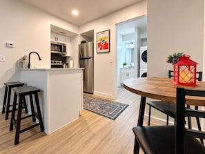 Une cuisine moderne dotée d’un îlot central, d’appareils électroménagers en acier inoxydable et d’un coin repas avec une table ronde en bois et des chaises noires.