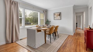 A dining area with a table set for four, a white armchair, and a red cabinet. - Gilded Renegade Retreat - Walk to Doak, Sleeps 10 (Tallahassee)