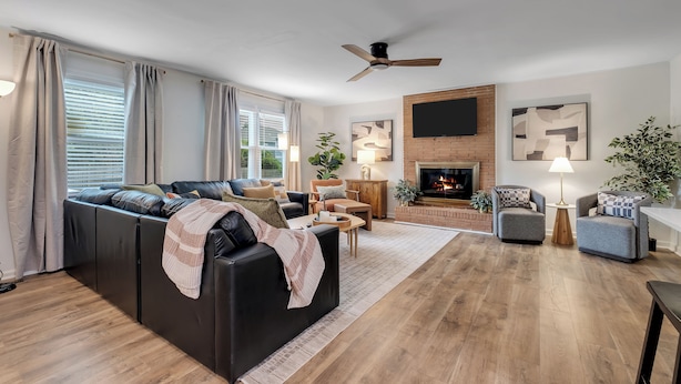 A modern living room with a black leather sofa, a fireplace, and a flat-screen TV mounted on a brick wall. - Gilded Renegade Retreat - Walk to Doak, Sleeps 10 (Tallahassee)