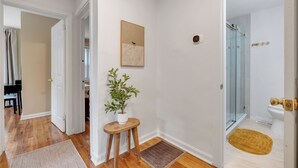 A hallway with a wooden floor, a potted plant, a framed picture, and a glass shower door. - Gilded Renegade Retreat - Walk to Doak, Sleeps 10 (Tallahassee)