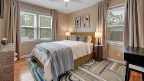 A bedroom with a bed, two bedside lamps, a ceiling fan, and a window with blinds. - Gilded Renegade Retreat - Walk to Doak, Sleeps 10 (Tallahassee)