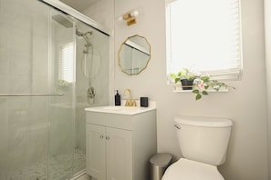 Un baño moderno con cabina de ducha de vidrio, inodoro blanco, tocador con grifo dorado y espejo con marco dorado.
