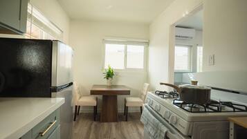 Cocina compacta equipada con refrigerador, estufa y mesa con sillas.