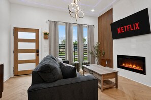 A modern living room with a sofa, a table, a fireplace, and a wall-mounted TV displaying 'NETFLIX'. - Modern 3BR for Teams, Work: Easy Highway Access (Houston)