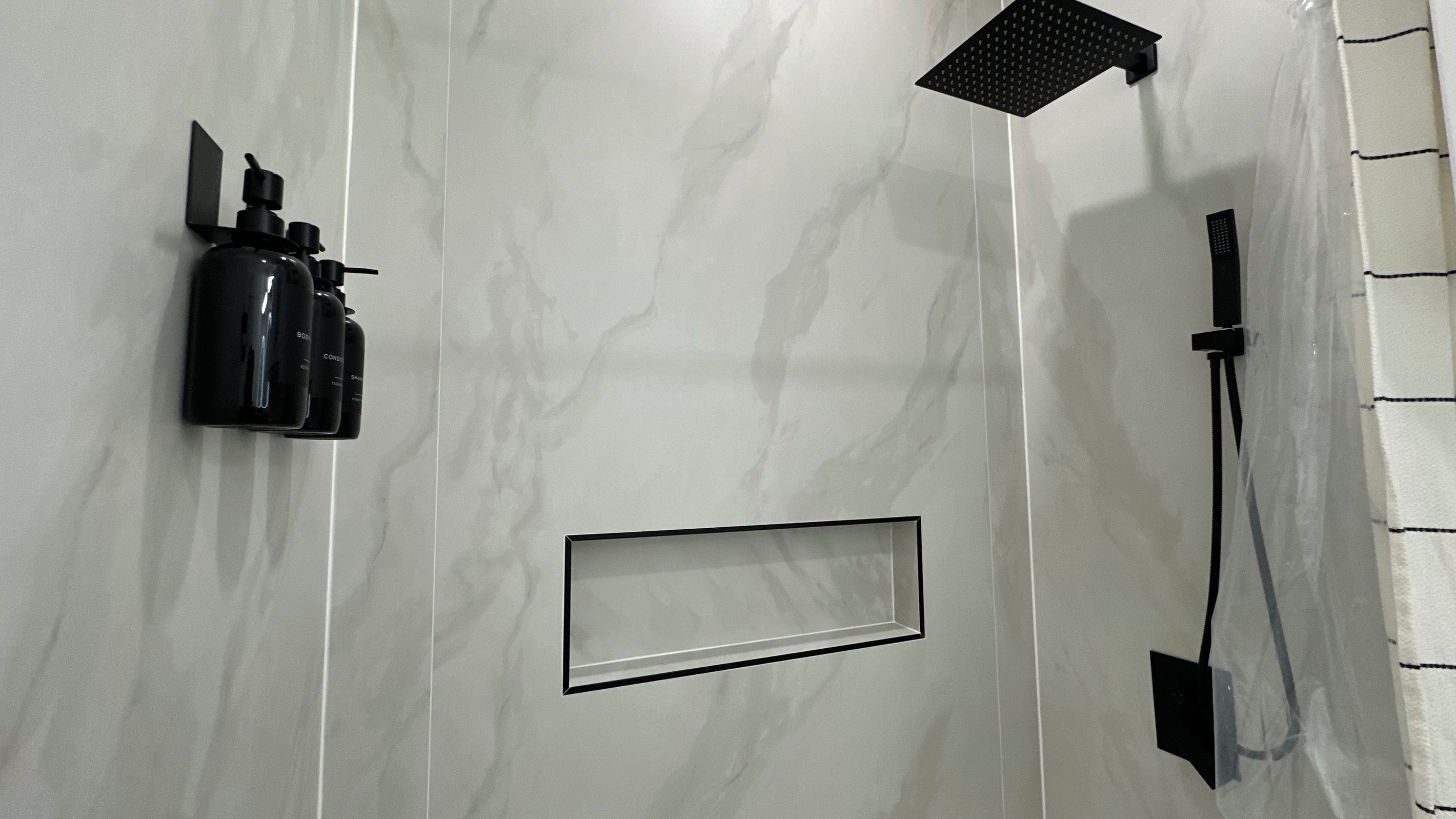A bathroom with a marble wall, a black soap dispenser, a showerhead, and a towel rack.