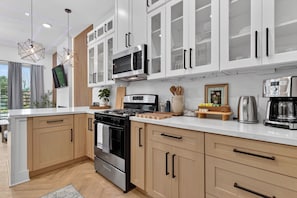 A modern kitchen with white cabinets, a built-in microwave, a stove, and a coffee maker. - Modern 3BR for Teams, Work: Easy Highway Access (Houston)