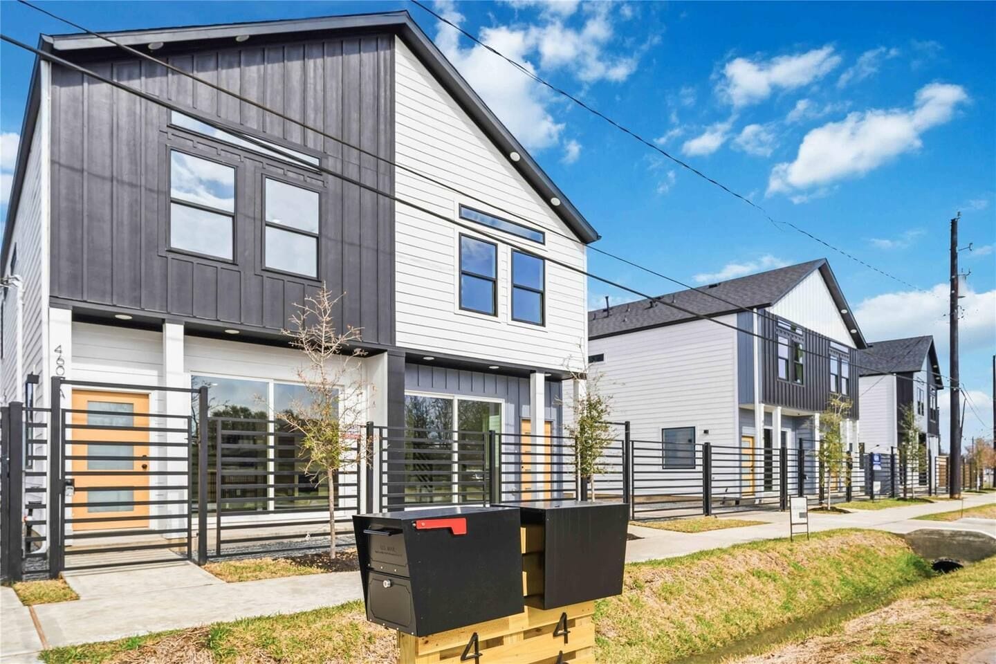 A modern two-story residential building with a grey and white exterior, a gated driveway, and a mailbox.