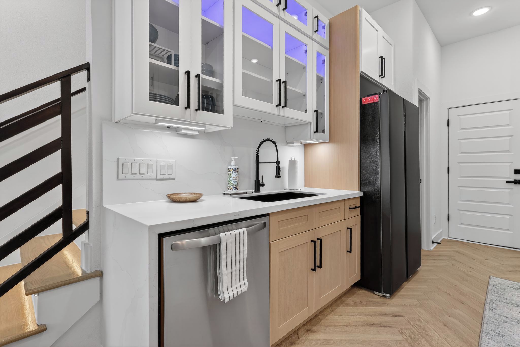 A modern kitchen with a built-in dishwasher, a black refrigerator, and a white countertop.