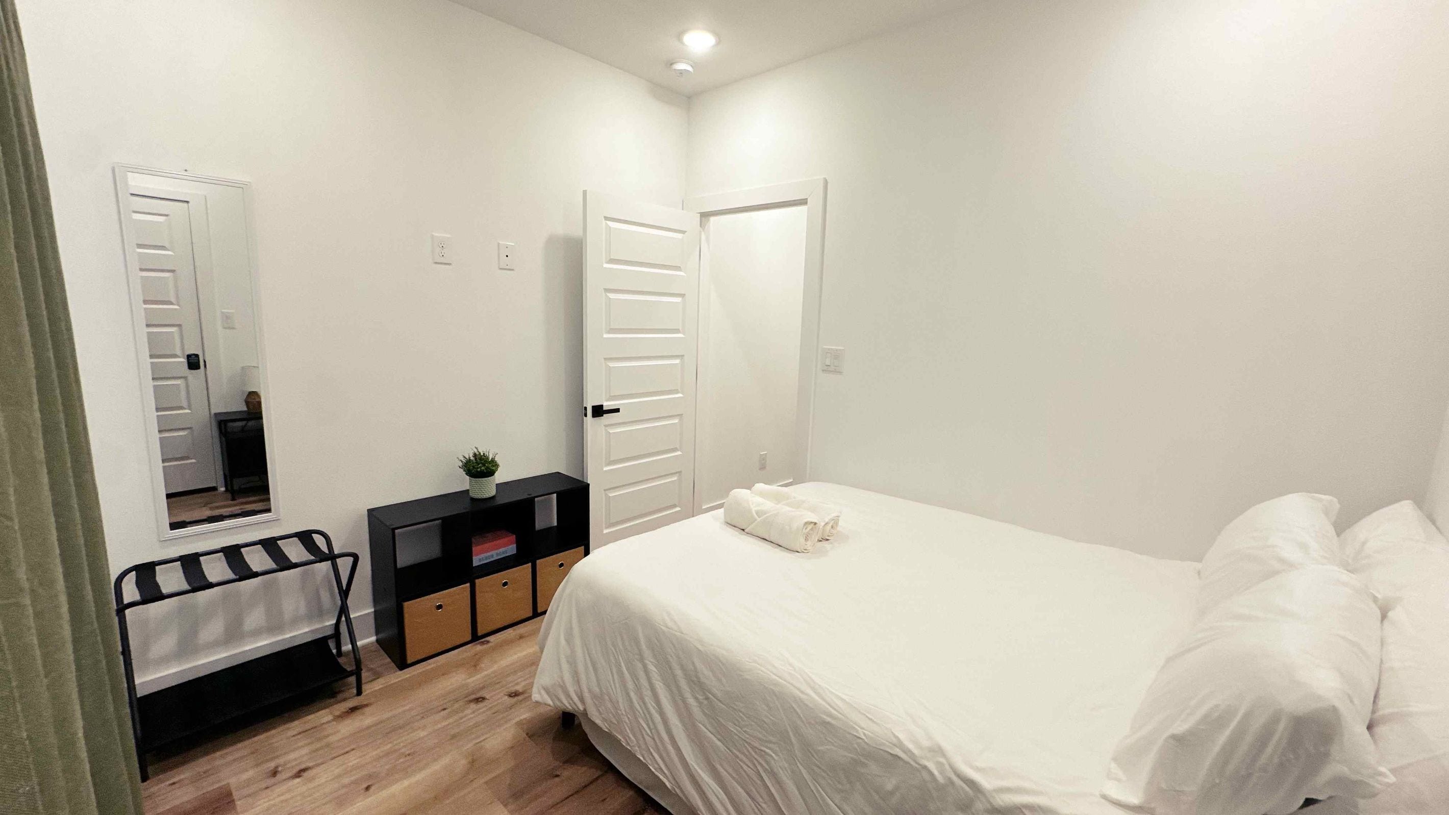 A bedroom with a bed, a bedside table, a mirror, and a wardrobe.