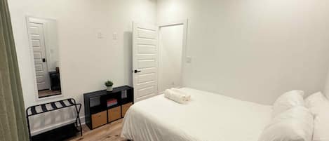 A bedroom with a bed, a bedside table, a mirror, and a wardrobe.