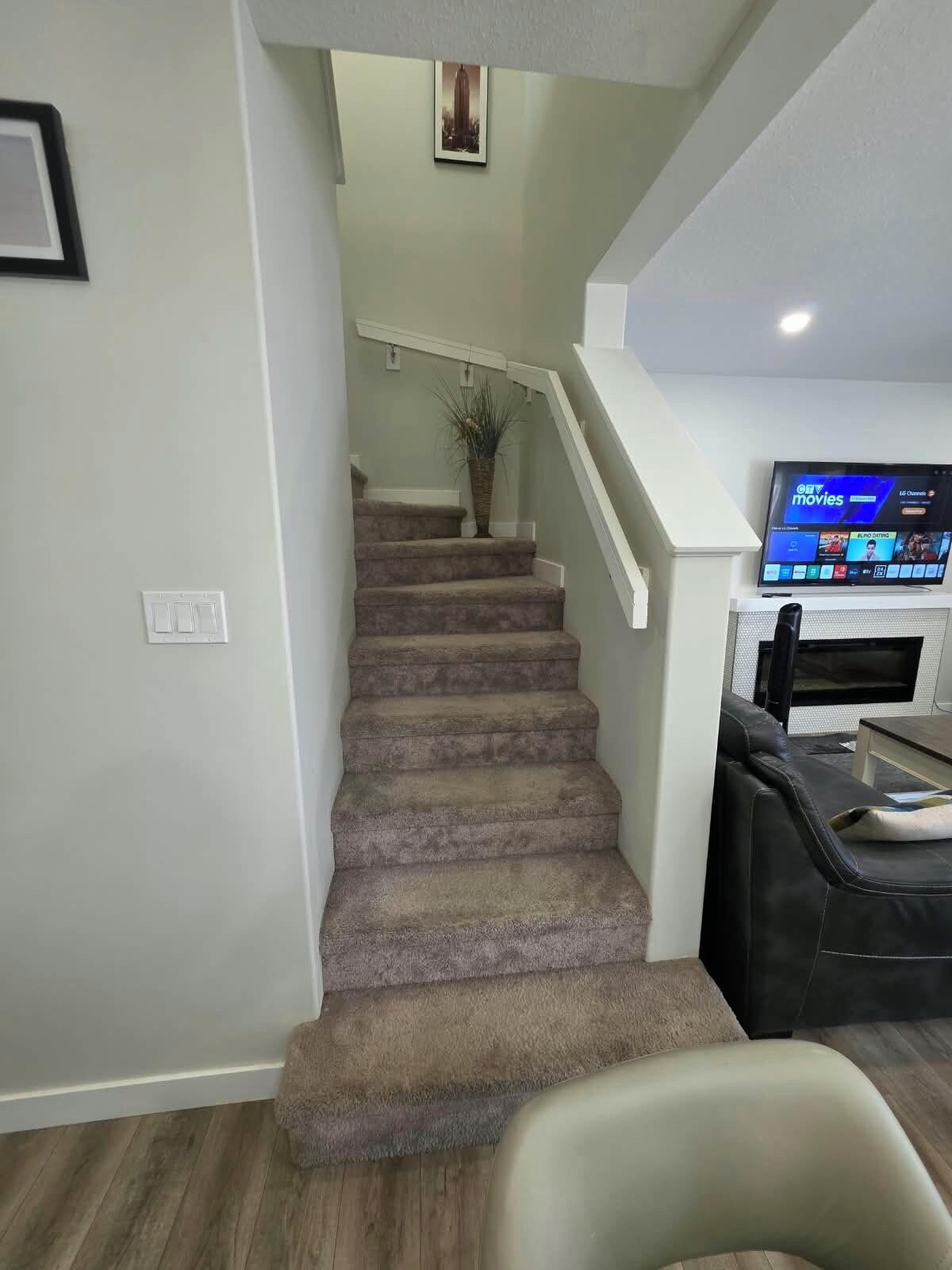 Un escalier menant à un deuxième étage, un téléviseur à écran plat fixé au mur et une petite table avec une chaise.