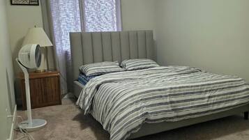 A bedroom with a bed, a bedside lamp, a small table, and a window with curtains.
