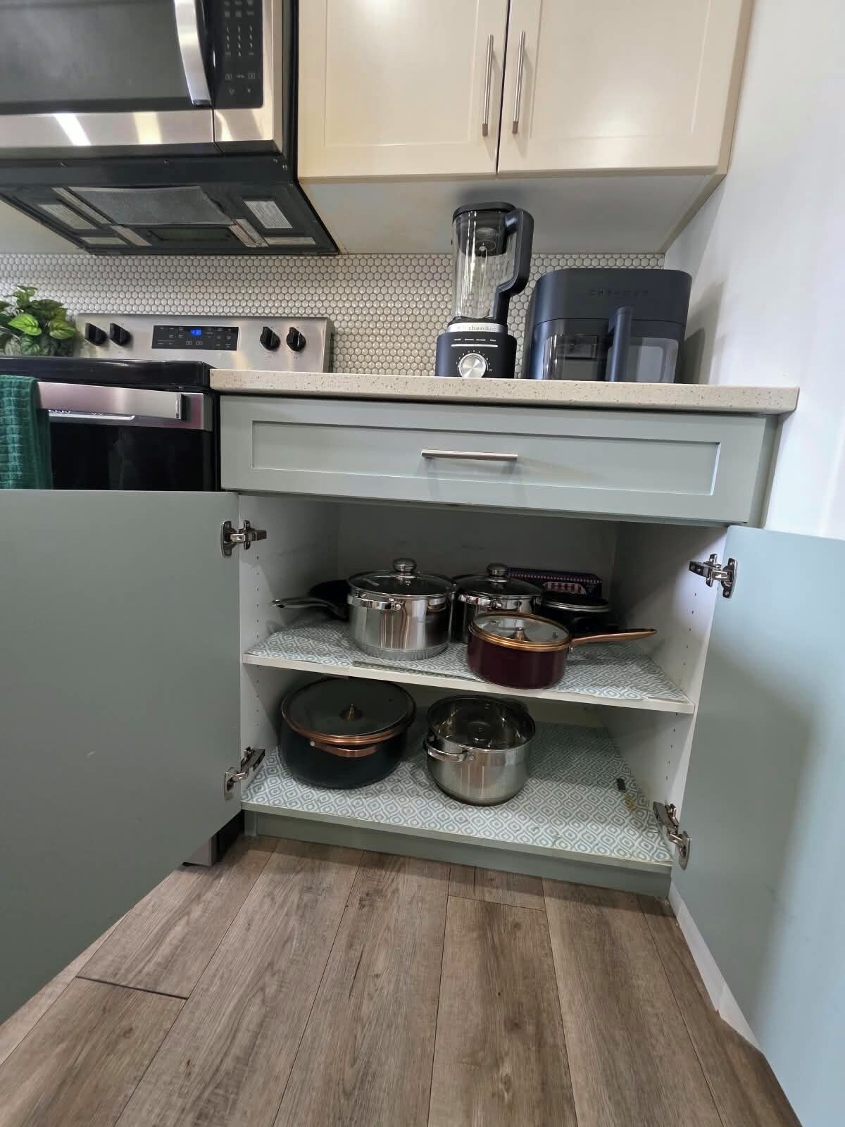 A compact kitchen with a microwave, coffee maker, and a shelf with pots.