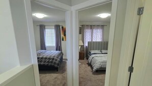 Un couloir menant à deux chambres dotées de moquettes et de murs blancs.