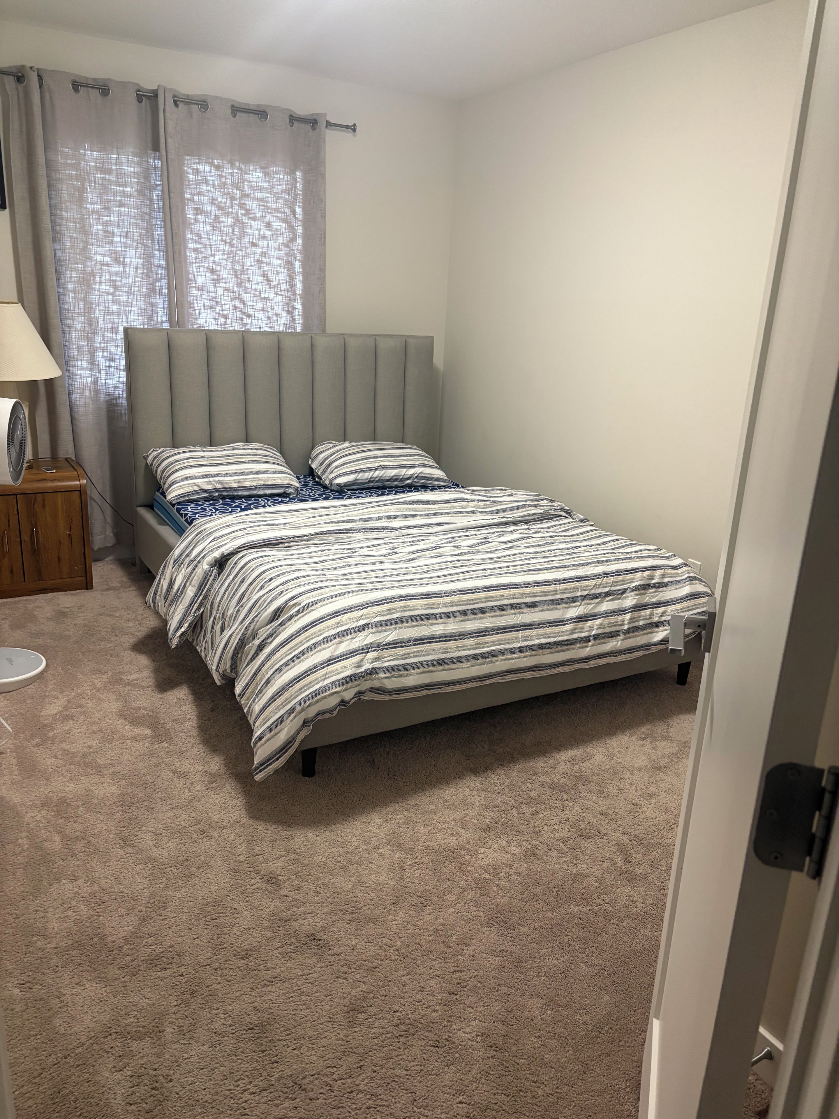 Un dormitorio con una cama, una mesita de noche, una lámpara y una ventana con cortinas.