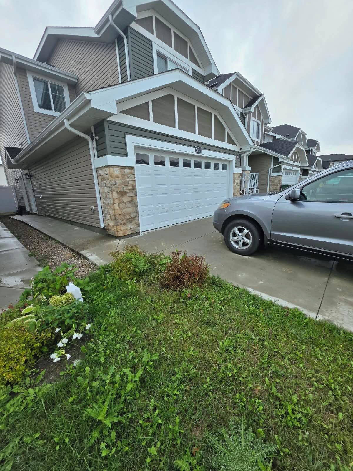 Une maison moderne à deux étages, dotée d’un garage, d’une allée et d’une voiture garée devant.