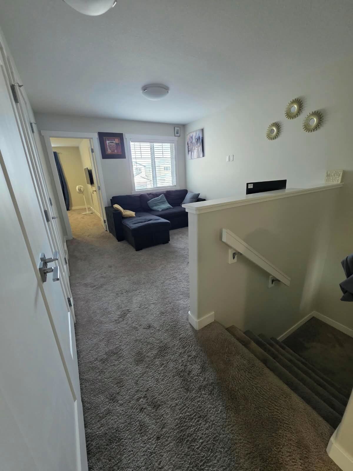 Ein Wohnzimmer mit einem dunkelgrauen Sofa, einer weißen Wand mit Dekoration und einer Treppe, die eine weitere Ebene hinaufführt.