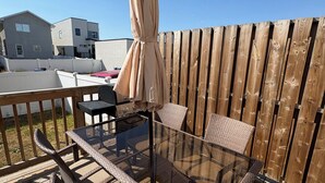 Une terrasse dotée de meubles en osier, d’une table en verre et d’un parasol beige.