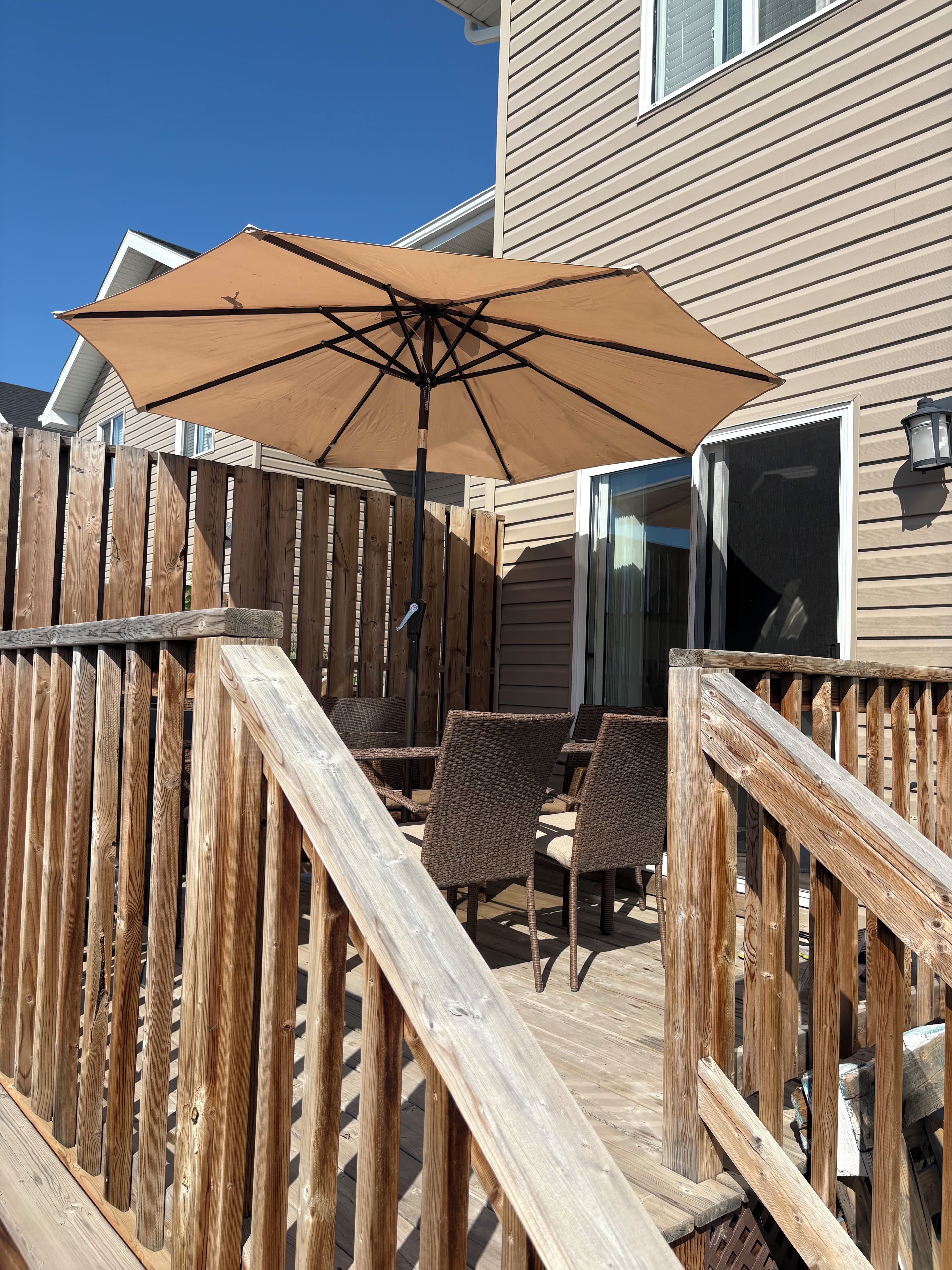 Une terrasse en bois avec un parasol, des chaises en osier et une clôture en bois.