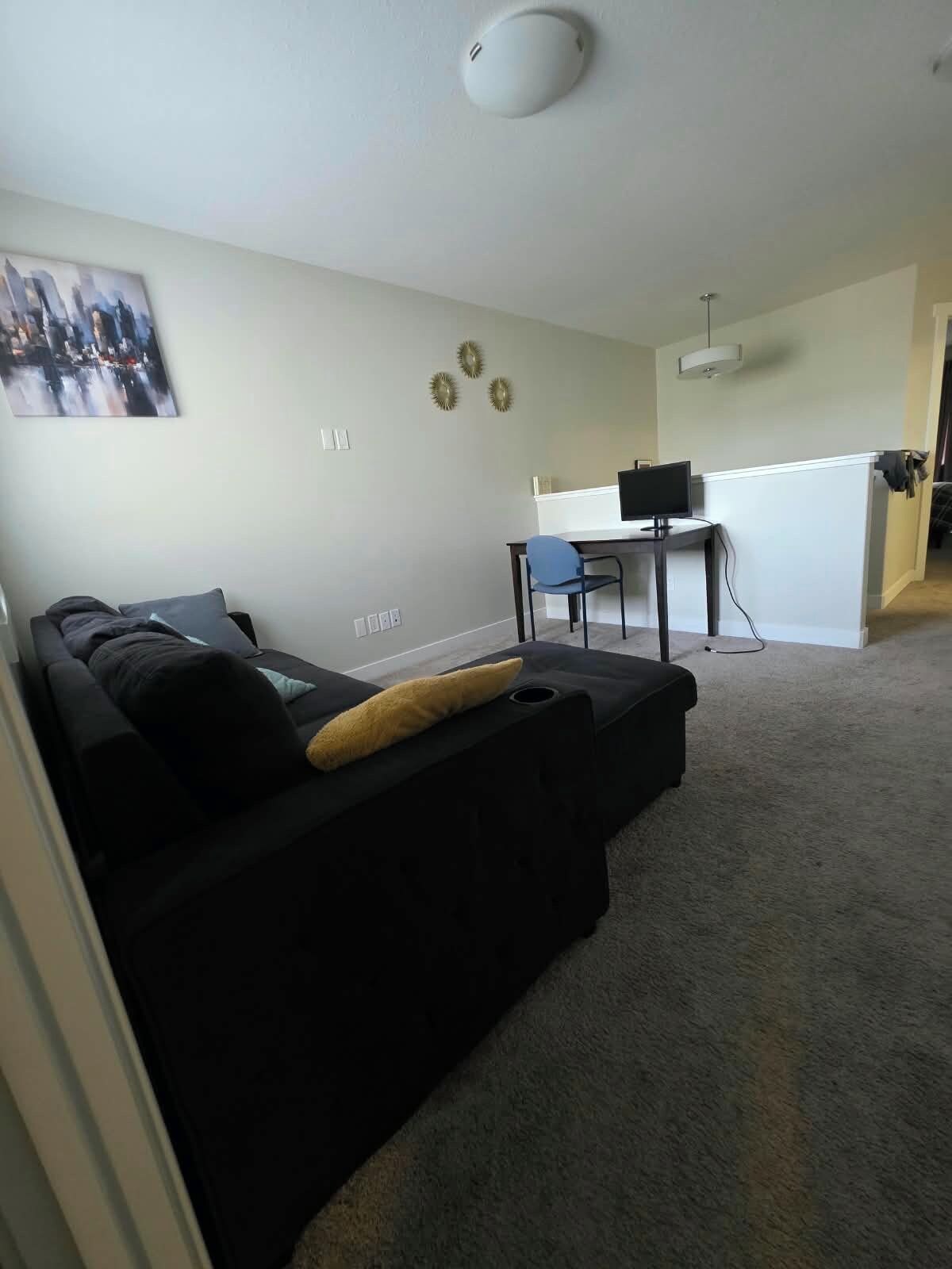 Ein modernes Wohnzimmer mit einem schwarzen Sofa, einem Schreibtisch mit einem Computer und einem Stadtbild an der Wand.