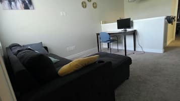 Ein modernes Wohnzimmer mit einem schwarzen Sofa, einem Schreibtisch mit einem Computer und einem Stadtbild an der Wand.