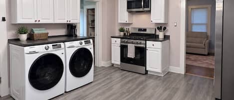 A modern kitchen with white cabinetry, a stainless steel refrigerator, a microwave, a stove, and a chandelier.
